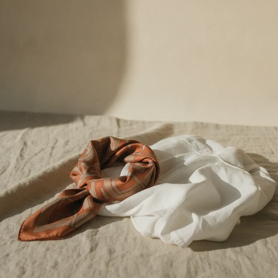 Un foulard de soie plie en carre pose a cote d une chemise blanche sur du lin