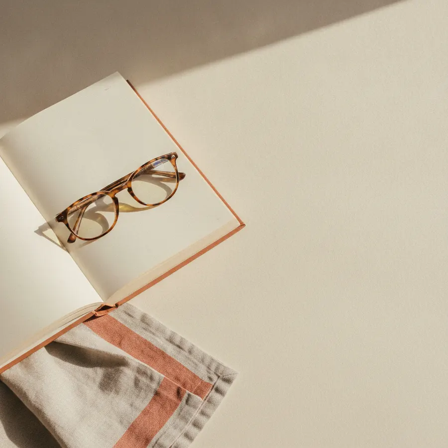 Une paire de lunettes a monture ecaille posee sur un livre ouvert, lumiere de fenetre