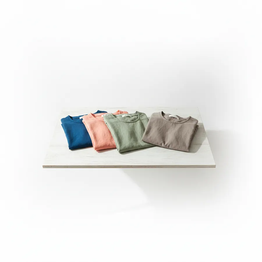 Trois hauts posés à plat sur une table de bois clair, un bleu canard, un corail doux et un vert amande, à côté d'un haut taupe éteint mis à l'écart