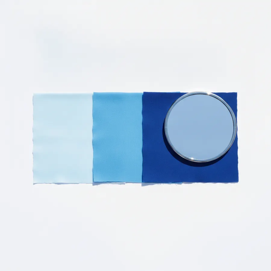 Trois echantillons de tissu bleu de saturations differentes, du bleu glacier au bleu roi profond, poses en ligne sur fond blanc a cote d'un miroir a main