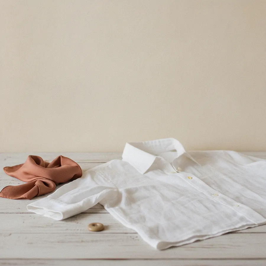 Une chemise blanche posee a plat, col releve tenant seul, sur une table de bois clair