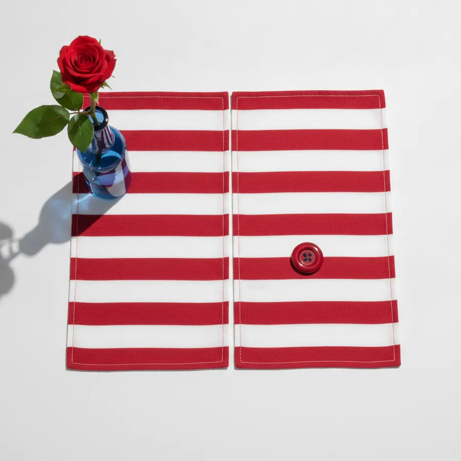 Deux panneaux de tissu a rayures horizontales rouges et blanches avec un bouton rouge sur le panneau droit, accompagnes d'un vase en verre bleu contenant une rose rouge a feuilles vertes, sur fond blanc