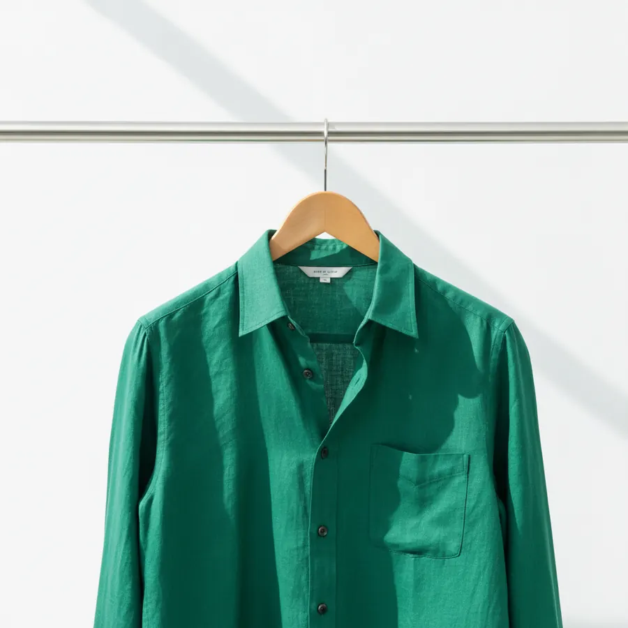 Un cintre en bois portant une chemise verte bien repassee, seul sur une tringle, sur fond blanc