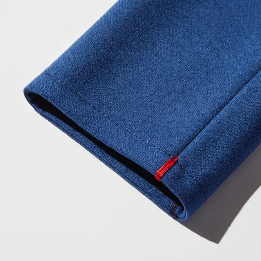 Un gros plan sur le bas d'une manche d'un vetement en tissu bleu, avec une petite etiquette rouge visible au niveau de l'ouverture de la manche