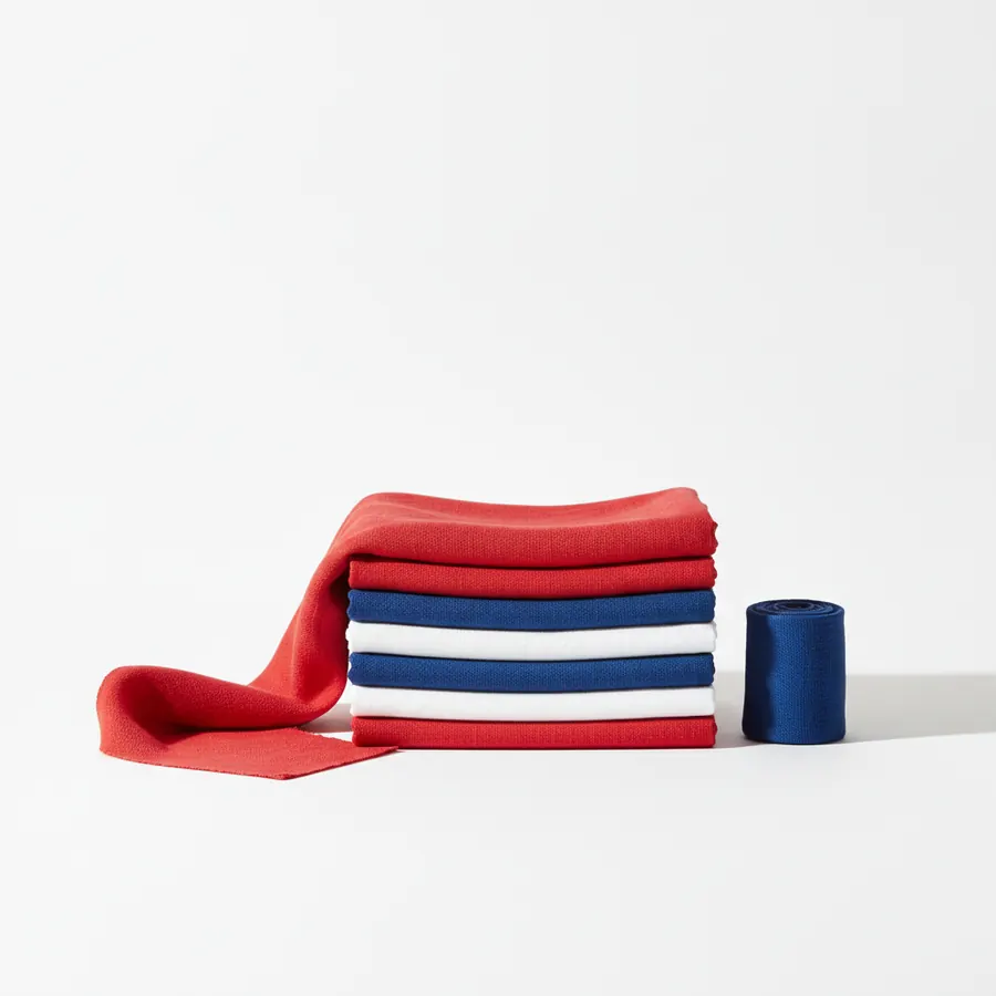 Une pile de tissus plies en rouge, bleu et blanc, avec une longue bande de tissu rouge depliee sur le cote gauche et un rouleau de ruban bleu marine a droite