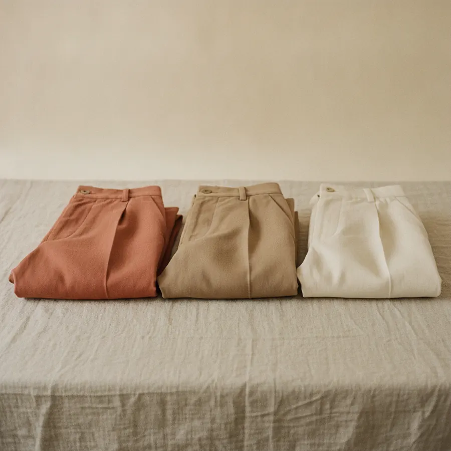 Trois pantalons plies cote a cote sur un drap de lin, une coupe droite, une coupe large et une coupe fuselee