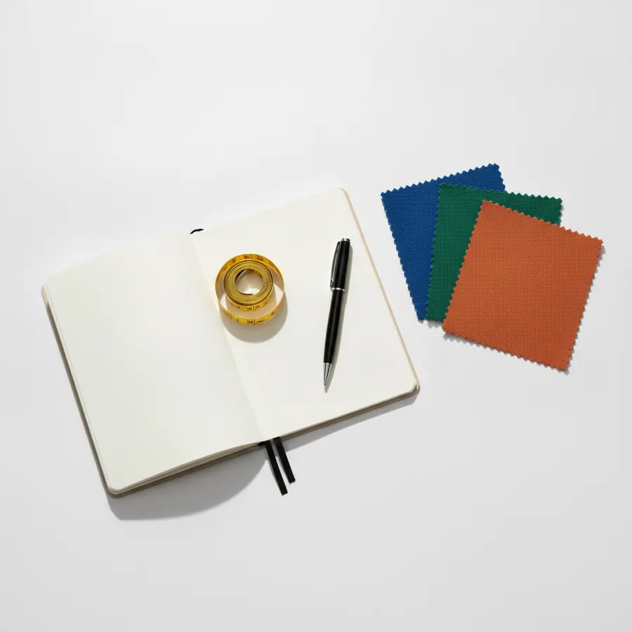 Un ruban a mesurer souple enroule pose a cote d'un carnet ouvert et d'un stylo, avec trois echantillons de tissu bleu, vert et terracotta, sur fond blanc