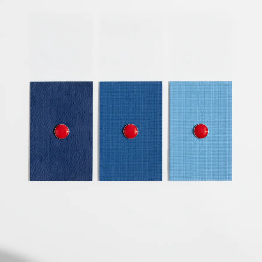 Trois rectangles de tissu bleu poses sur un fond gris clair, de gauche a droite dans des teintes allant du bleu marine au bleu ciel, chacun orne d'un bouton rond rouge au centre
