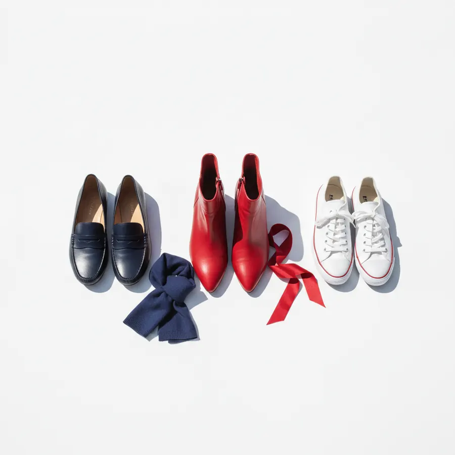 Trois paires de chaussures posées sur un fond blanc : à gauche, des mocassins bleu marine avec un nœud en tissu bleu marine ; au centre, des bottines pointues rouges avec un ruban rouge ; à droite, des baskets blanches à lacets blancs et liserés rouges