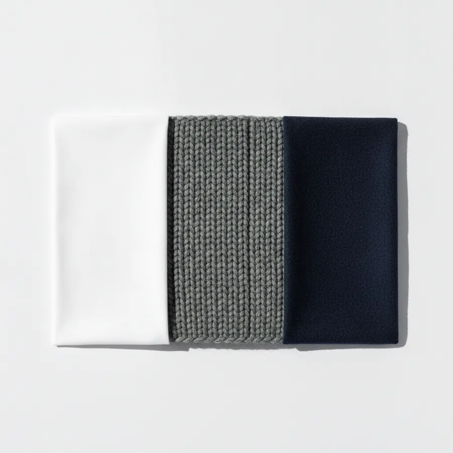Trois tissus posés bord à bord sur un fond blanc, un coton blanc lisse à gauche, une grosse maille de laine grise côtelée au centre et un lainage bleu marine mat à droite