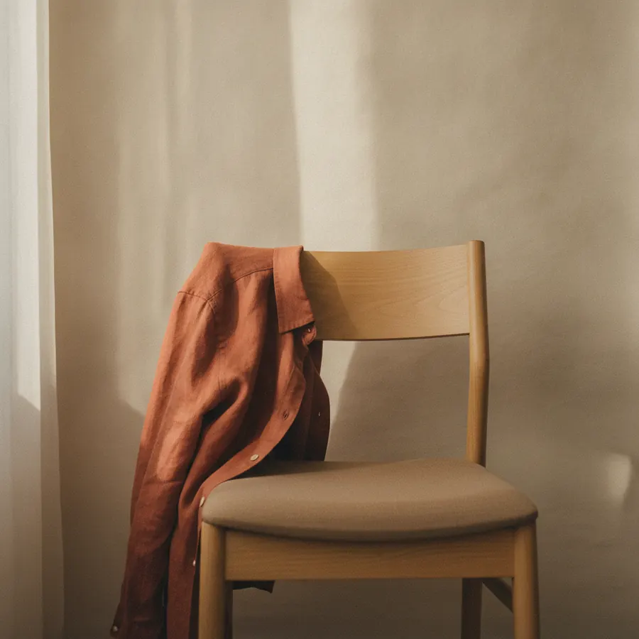 Un mur clair avec une chemise unie posee sur un dossier de chaise, lumiere de fenetre